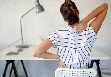 Overworked woman with back pain in office sitting on chair with bad posture