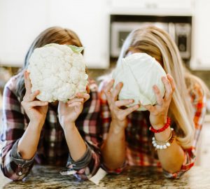 a couple women holding a cauliflower and cabbage
