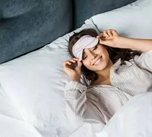 attractive happy girl in sleeping eye mask relaxing in bed in the morning