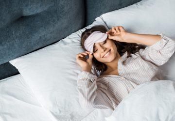 attractive happy girl in sleeping eye mask relaxing in bed in the morning